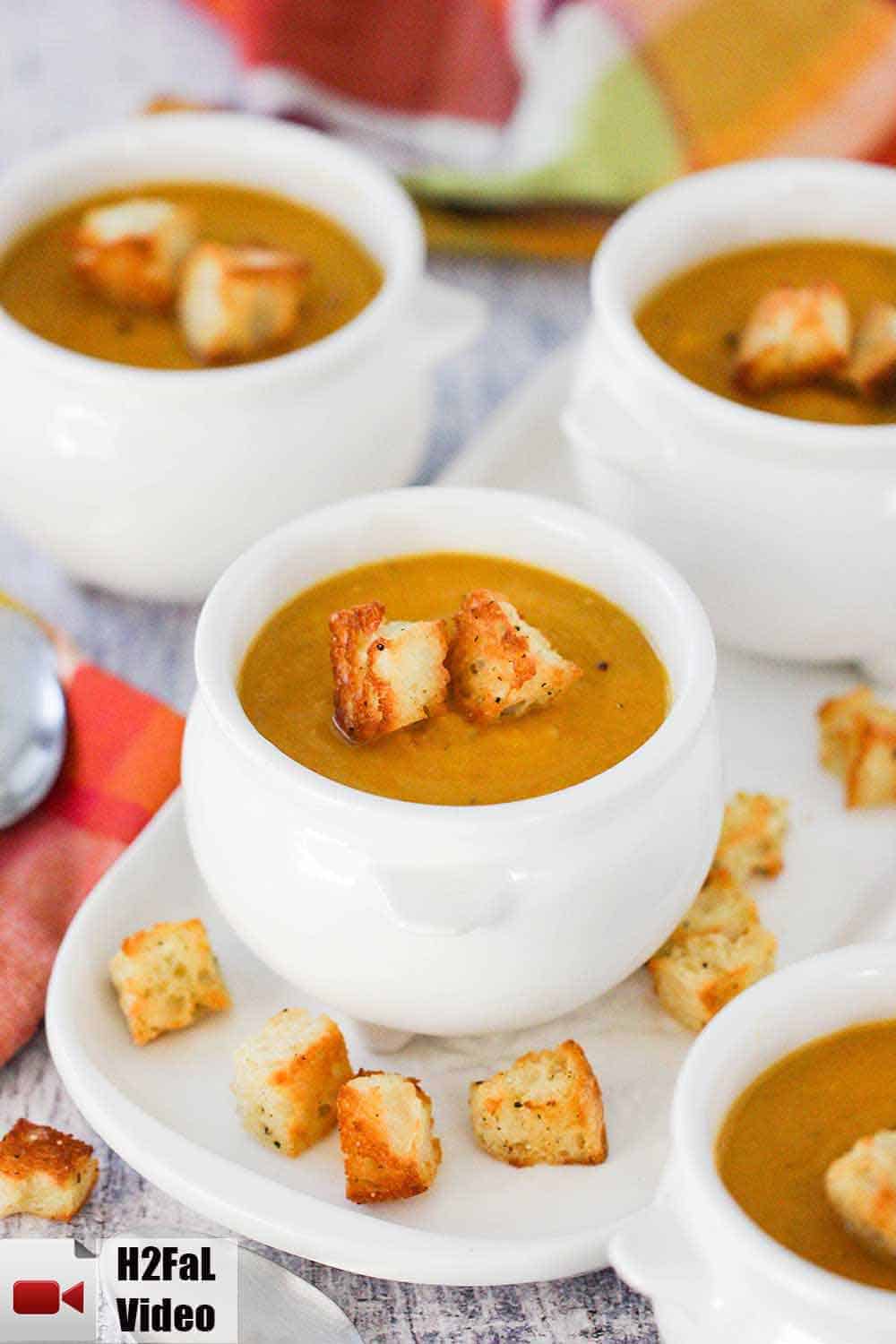 A small crock of roasted butternut squash on a small white plate with croutons on it. 