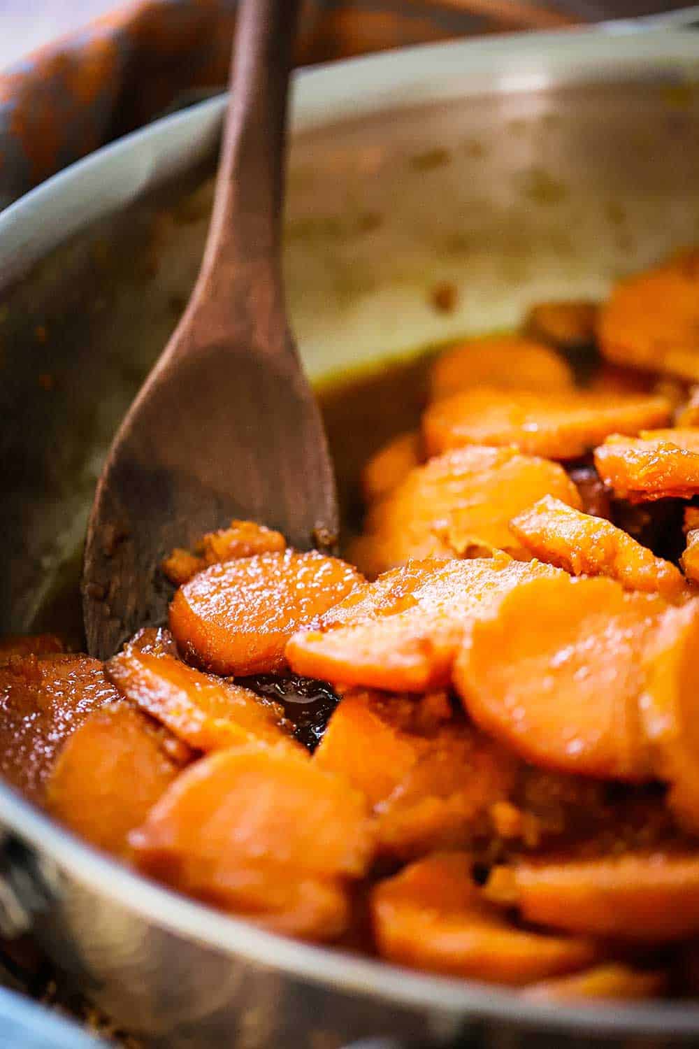 A large silver pan filled with candied yams and a wooden spoon. 