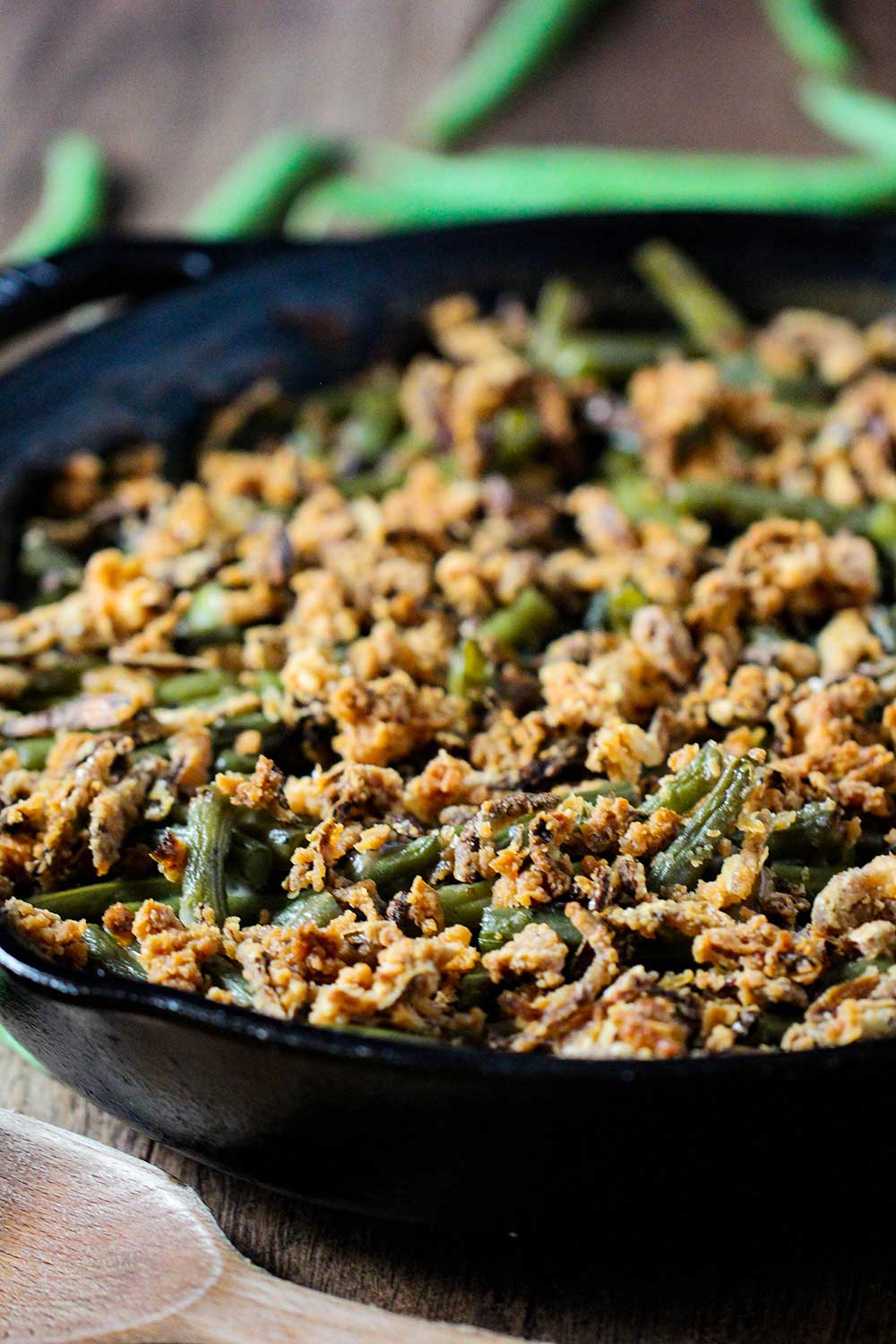 A large cast iron skillet holding gourmet green bean casserole with fresh green beans next to it. 