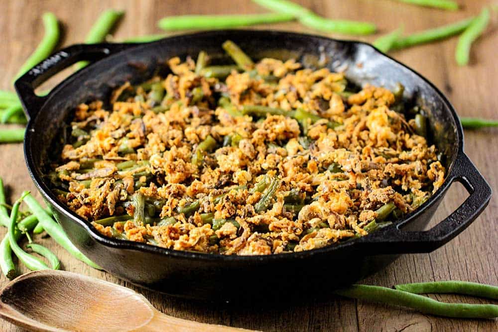 A large black cast iron skillet filled with green bean casserole with fresh green beans next to it. 