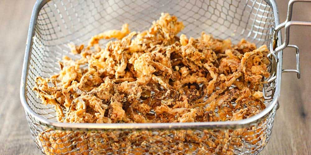 A fryer basket filled with fried onion strips. 