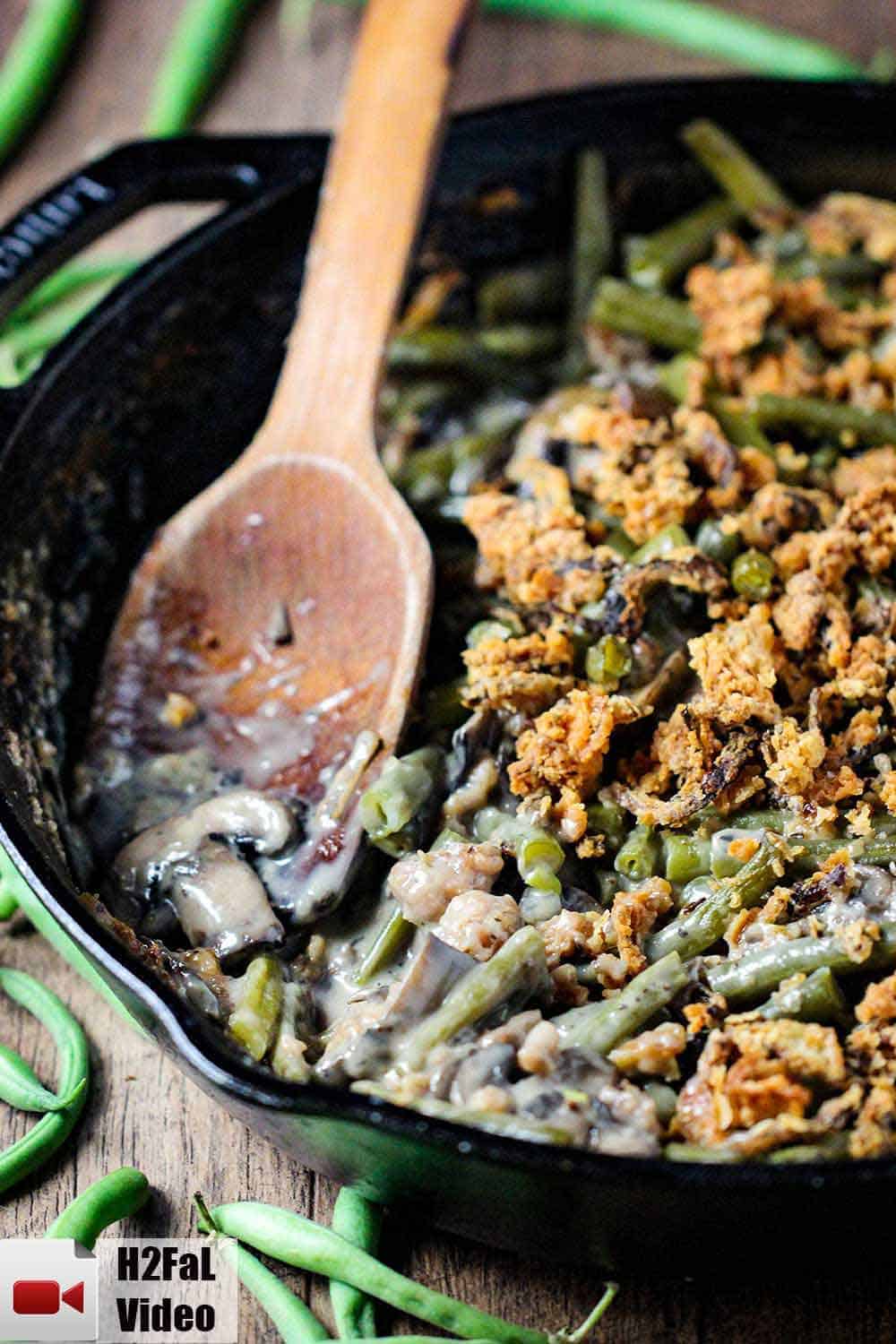 A large black cast iron skillet filled with gourmet green bean casserole with a wooden spoon in it. 