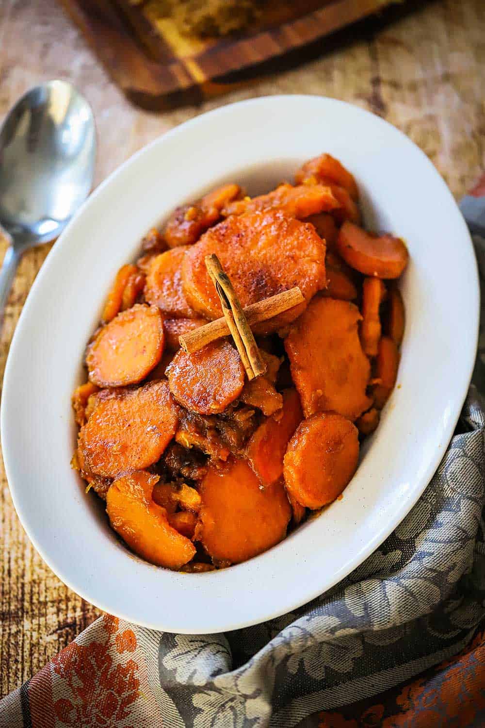 An oval serving dish filled with classic candied yams with two cinnamon sticks crossed on top. 