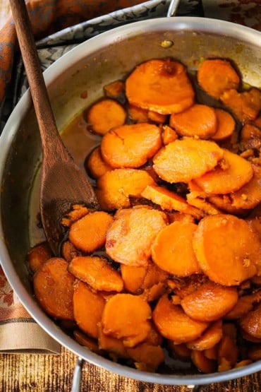 A large silver skillet filled with cooked candied yams and wooden spoon.