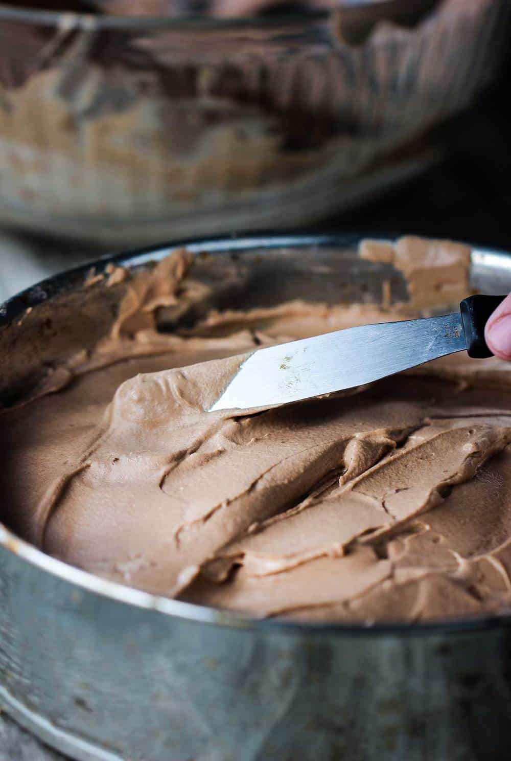 Spreading chocolate mousse onto shortbread crust in pan.