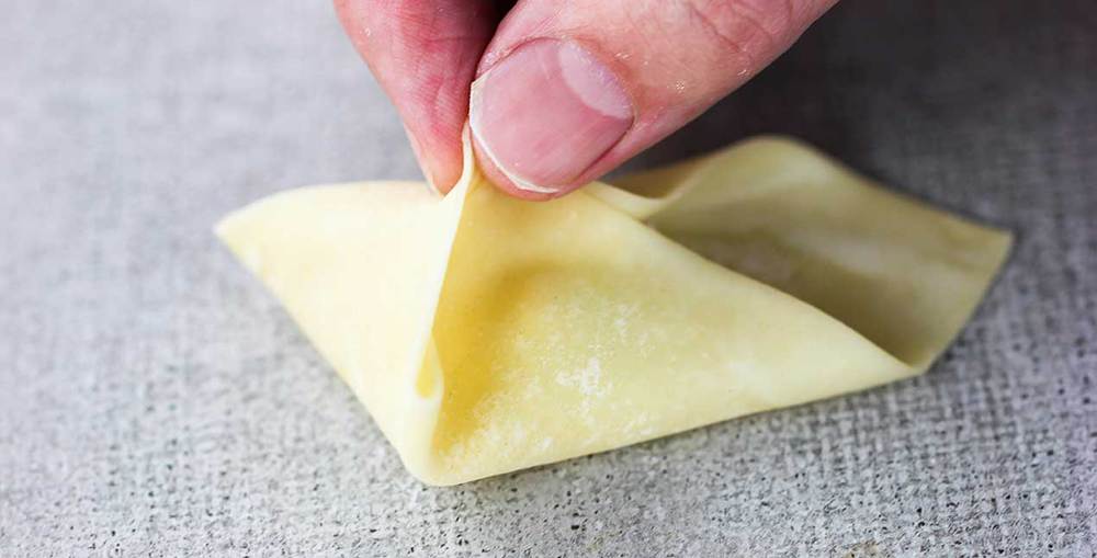 Fingers pinching one side of a wonton wrapper for a crab rangoon