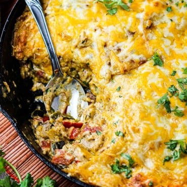 King Ranch casserole in a large cast iron skillet with a spoon in it all next to festive napkins.