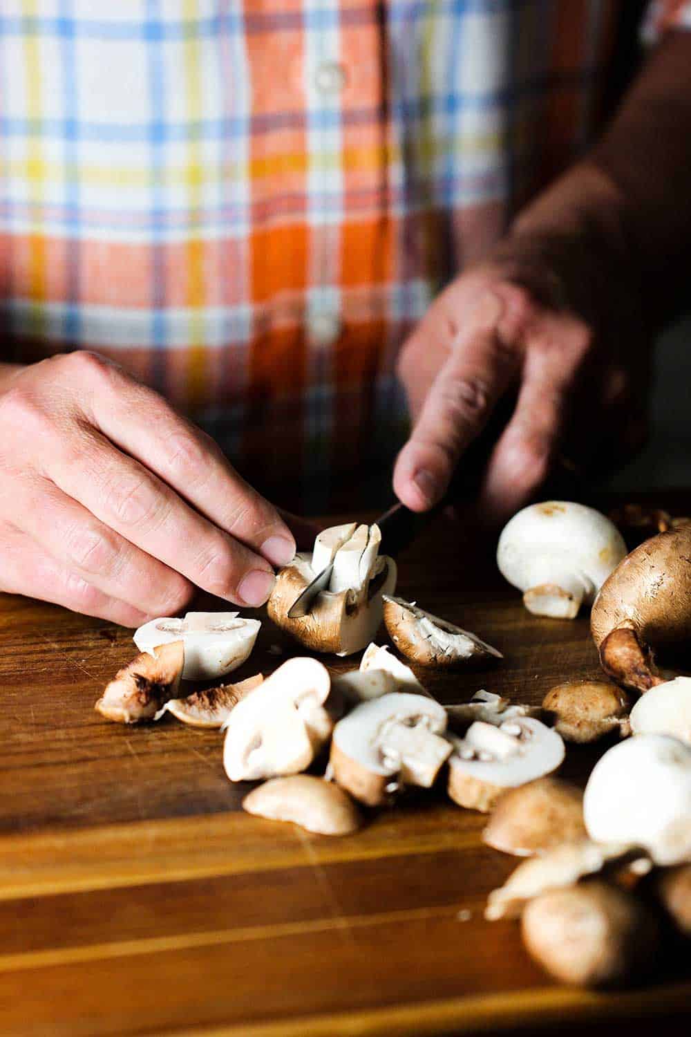 Two hands using a knife to slice mushrooms for chicken and sage casserole. 