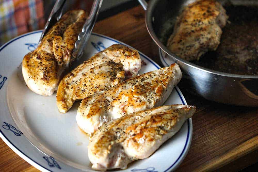 A pair of tongs placing seared chicken breasts on a platter. 