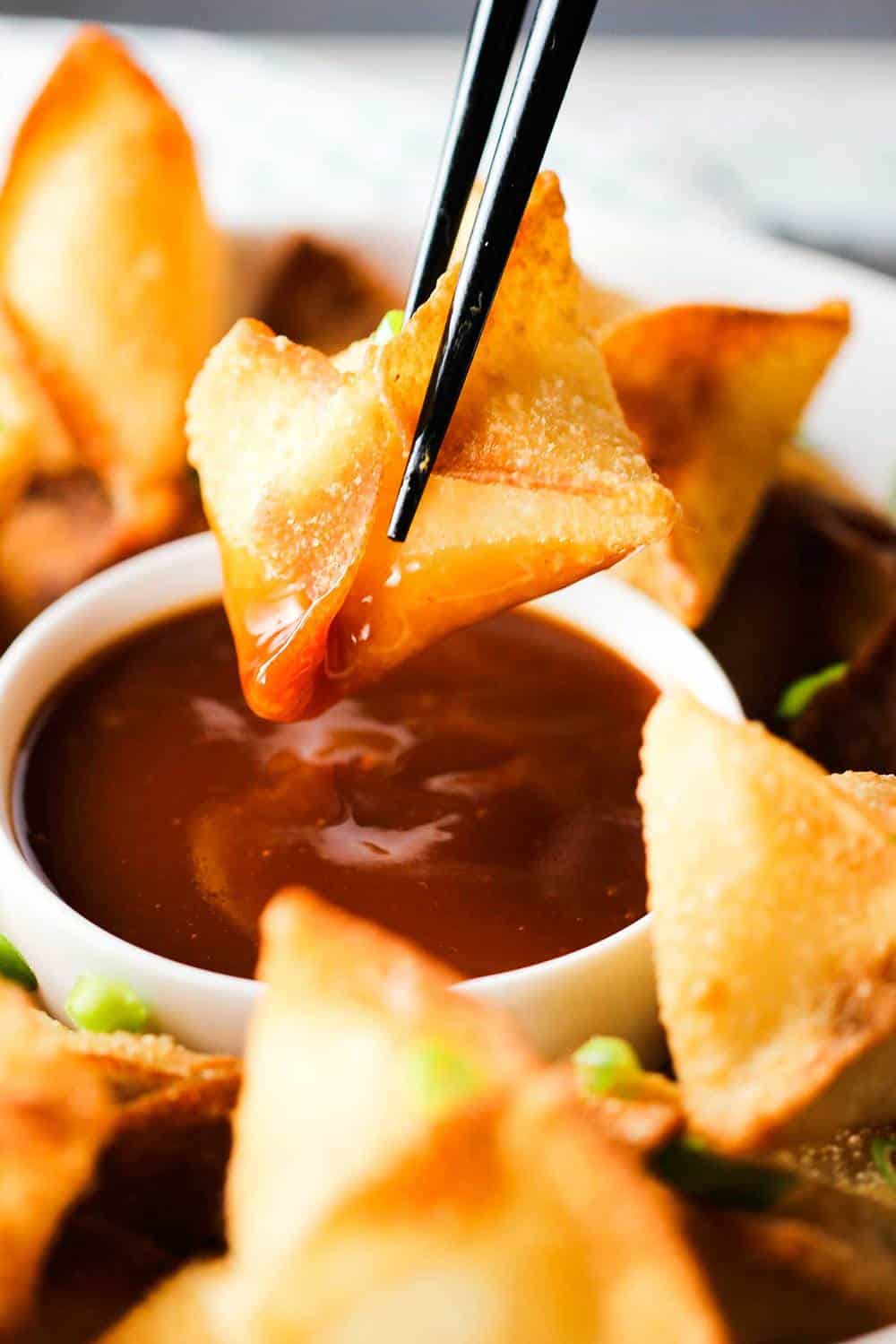 A crab rangoon being dipped into sauce with chop sticks