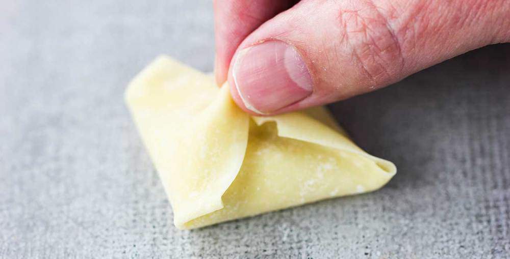 A crab rangoon being held together before cooked