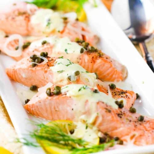 Poached salmon with capers and hollandaise sauce on a white platter