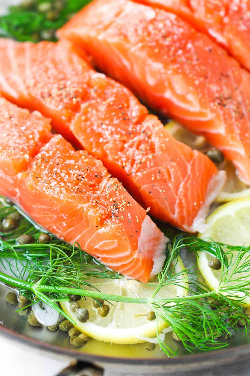 Fresh salmon in a skillet with aromatics for poached salmon