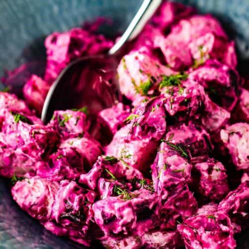 Roasted beet and potato salad with dill dressing in a blue bowl with a silver serving spoon