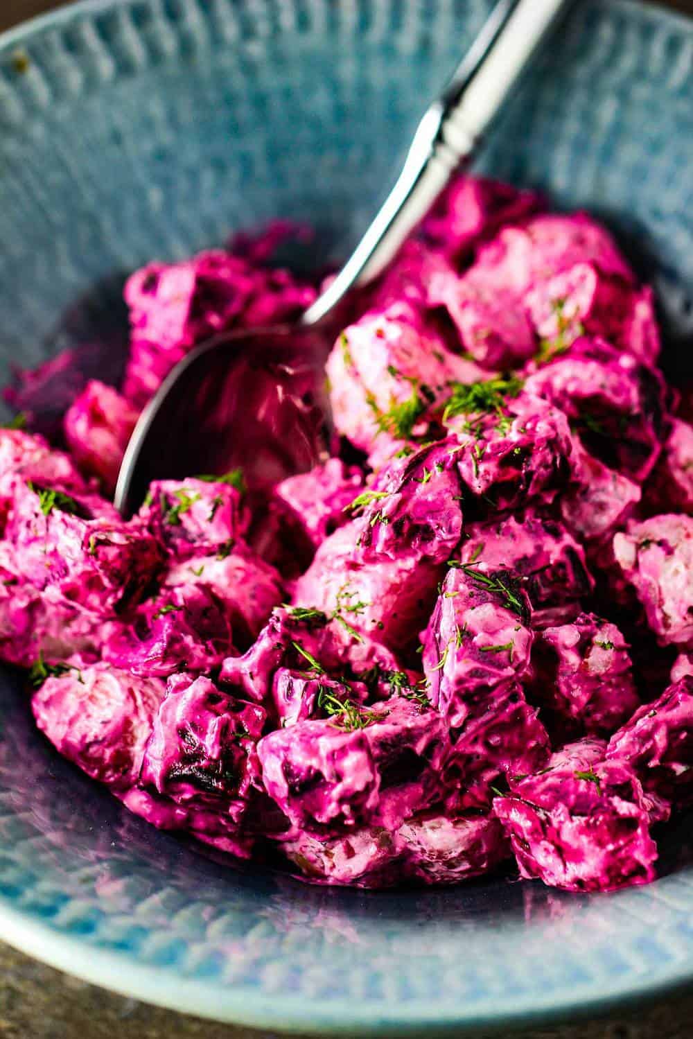 Roasted beet and potato salad with dill dressing in a blue bowl with a silver serving spoon