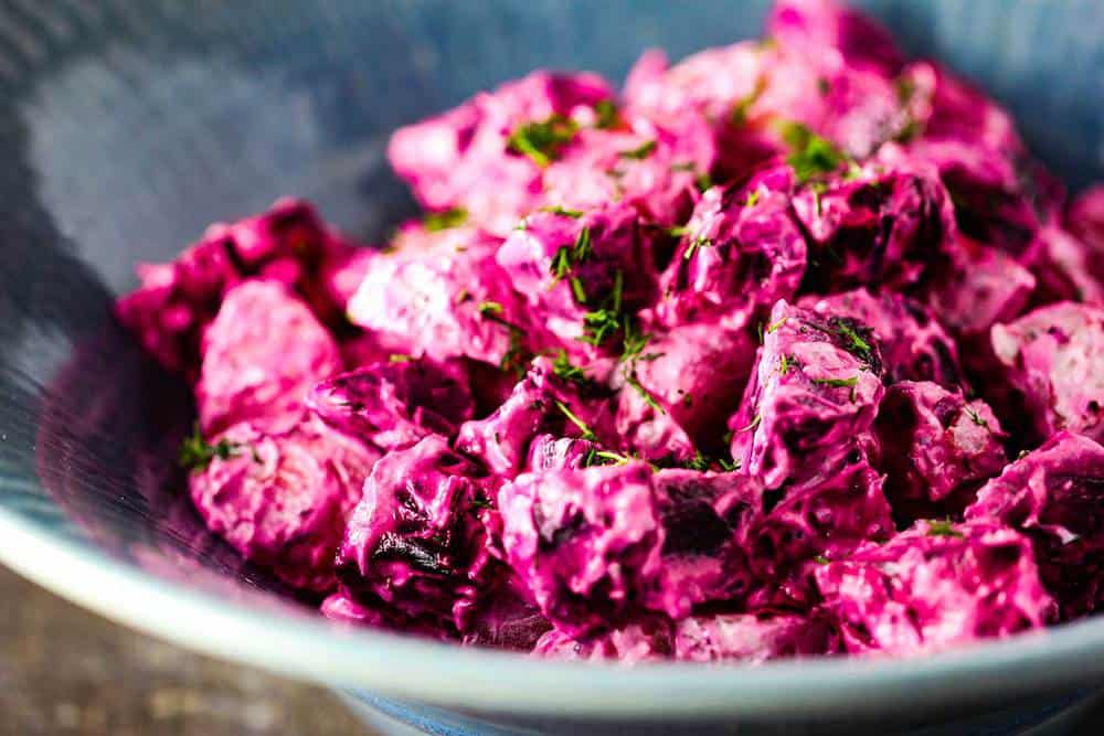 Roasted red beet and potato salad in a blue bowl with fresh dill on top