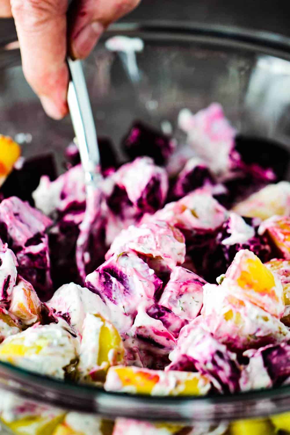 A spoon stirring together roasted beet and potato salad with dill dressing