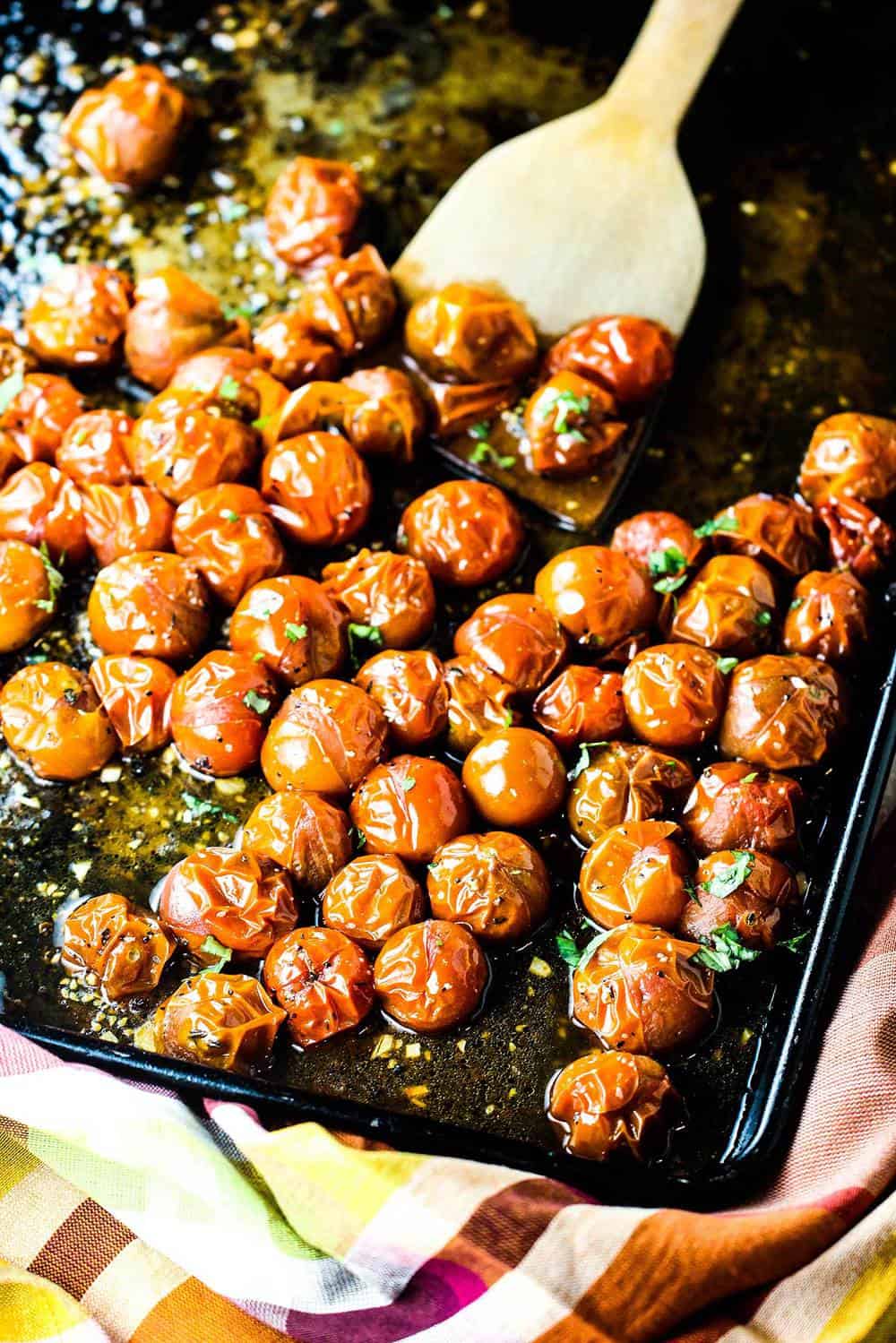 Roasted cherry tomatoes on a baking dish with a wooden spoon