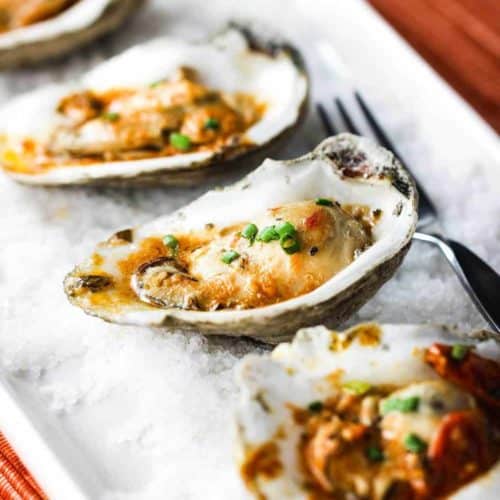 Grilled oysters with roasted tomato butter on a white dish with rock salt