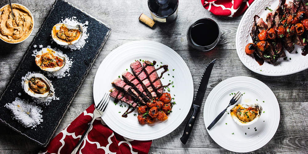 Grilled oysters and seared ribeye steak on a wooden table