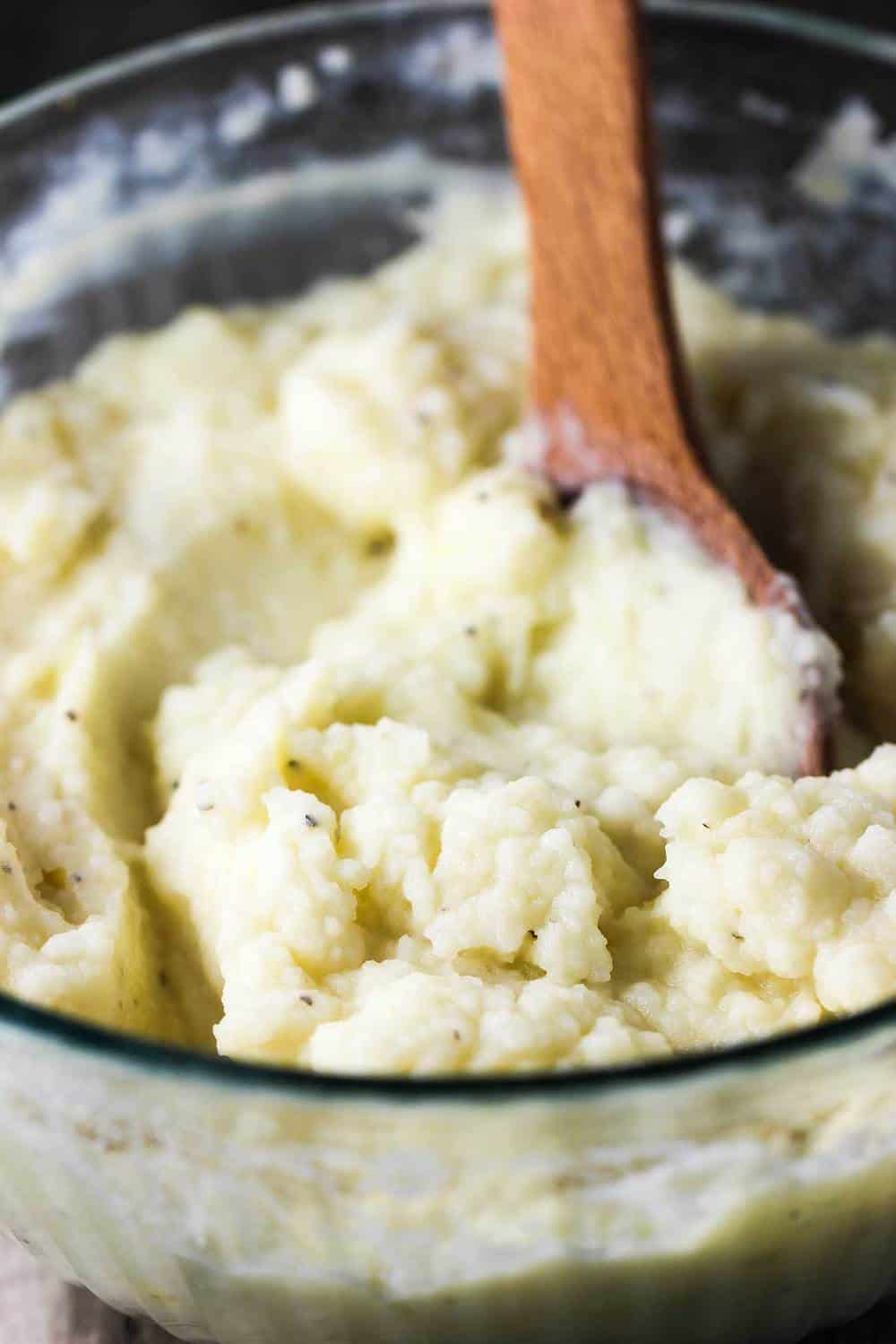 A bowl of whipped potatoes with a wooden spoon in it for shepherd's pie