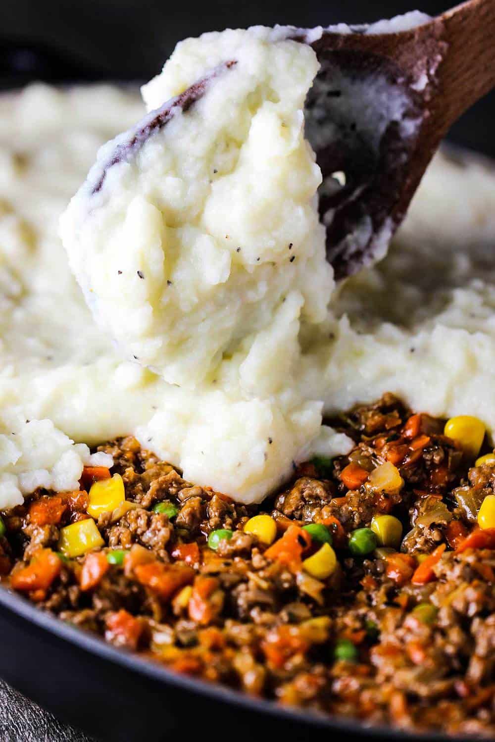 A wooden spoon adding a layer of whipped potatoes over meat filling for shepherd's pie