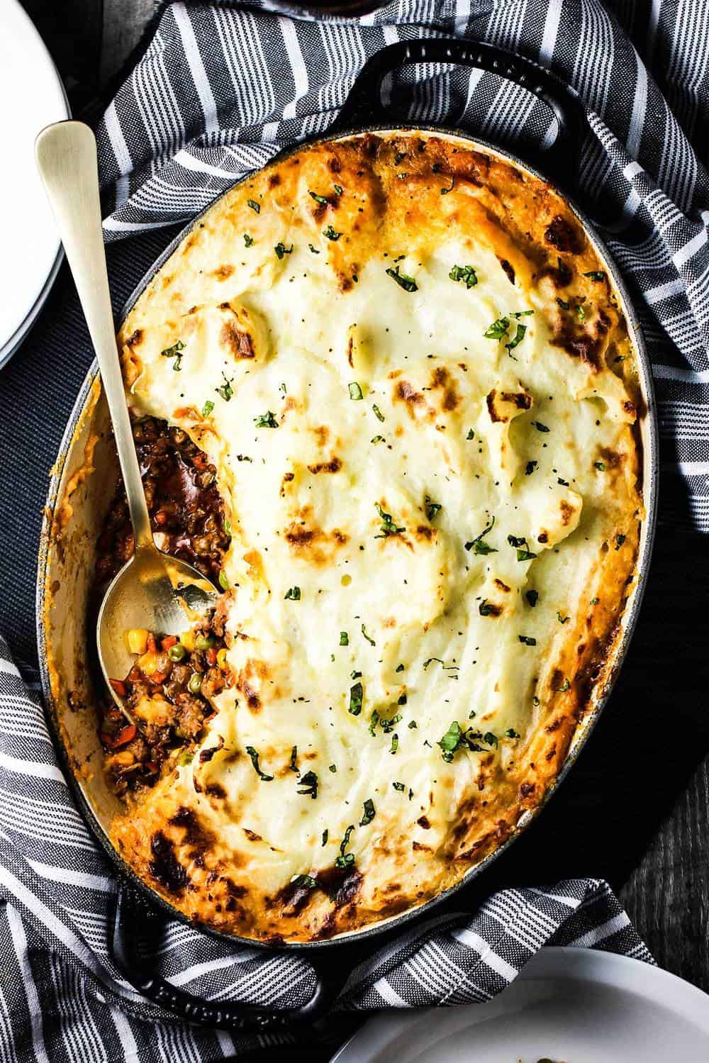 Homemade Sheperd's Pie in a black dish with a gold spoon in it. 