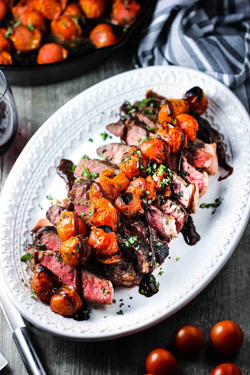 Sliced ribeye steak on a platter with roasted tomatoes and borderalaise sauce