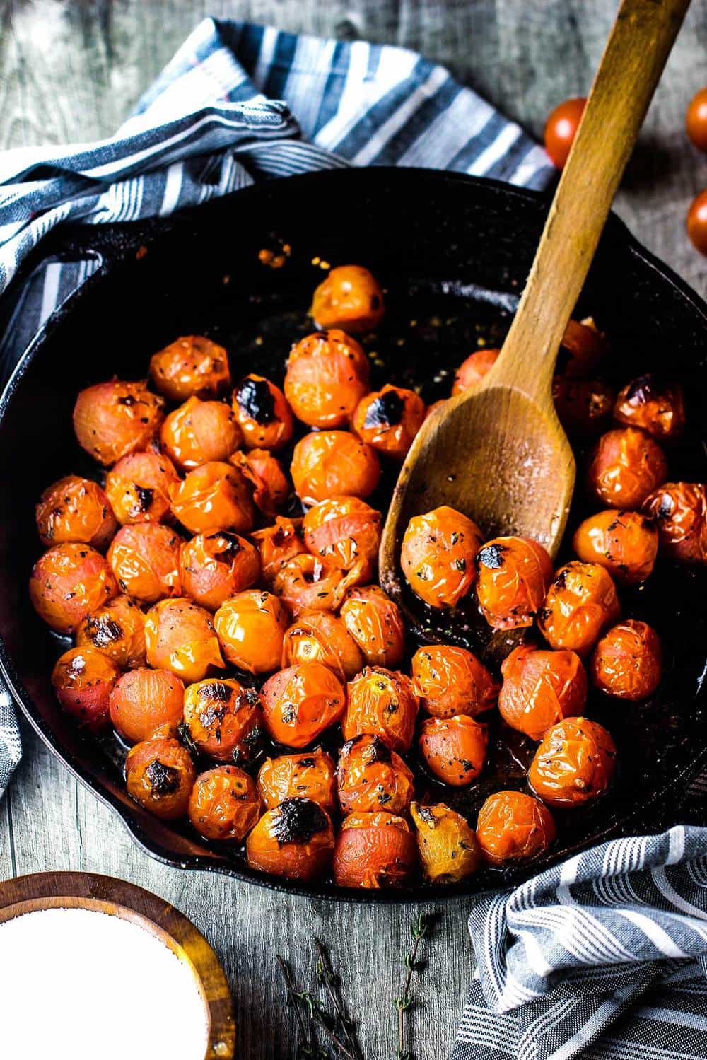 Blistered cherry tomatoes in a cast iron skillet with a wooden spoon