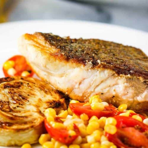 Sautéed Wild Striped Bass on a white plate with corn tomato salad and roasted fennel.