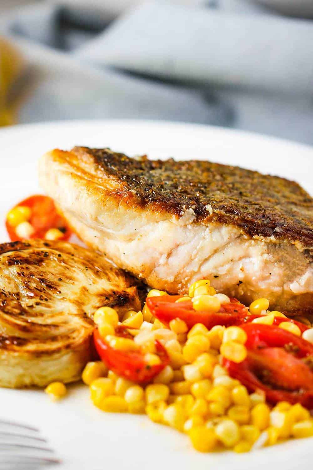 Sautéed Wild Striped Bass on a white plate with corn tomato salad and roasted fennel.