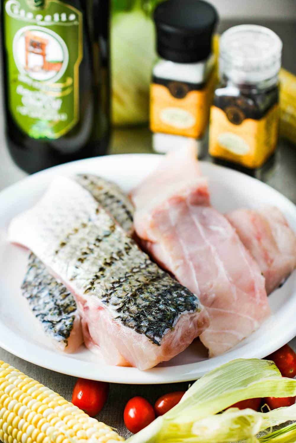 A plate of fresh uncooked wild striped bass and other ingredients around it. 