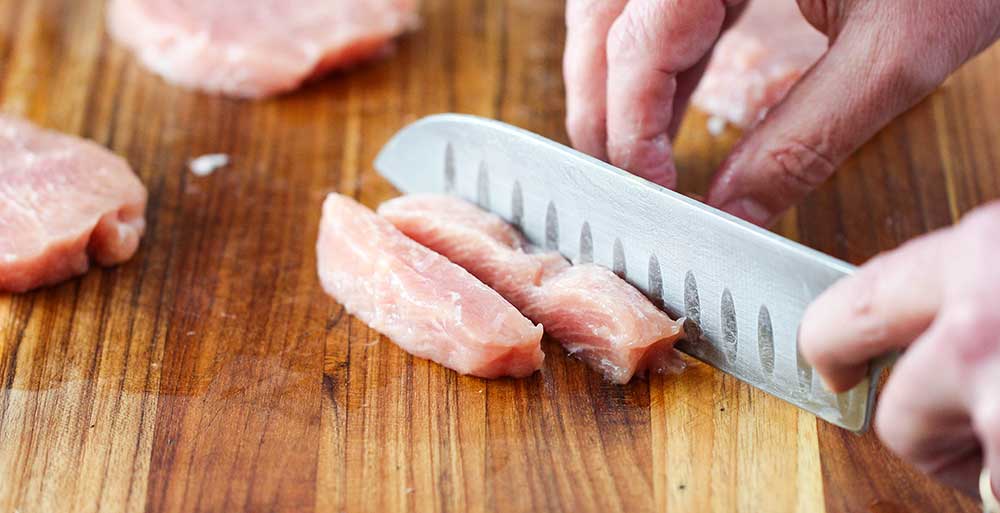 A hand and knife cutting a pork tenderloin into strips for Sweet and Sour Pork.