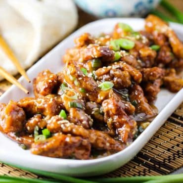 A white platter holding Sweet and Sour Pork with chop sticks nearby.