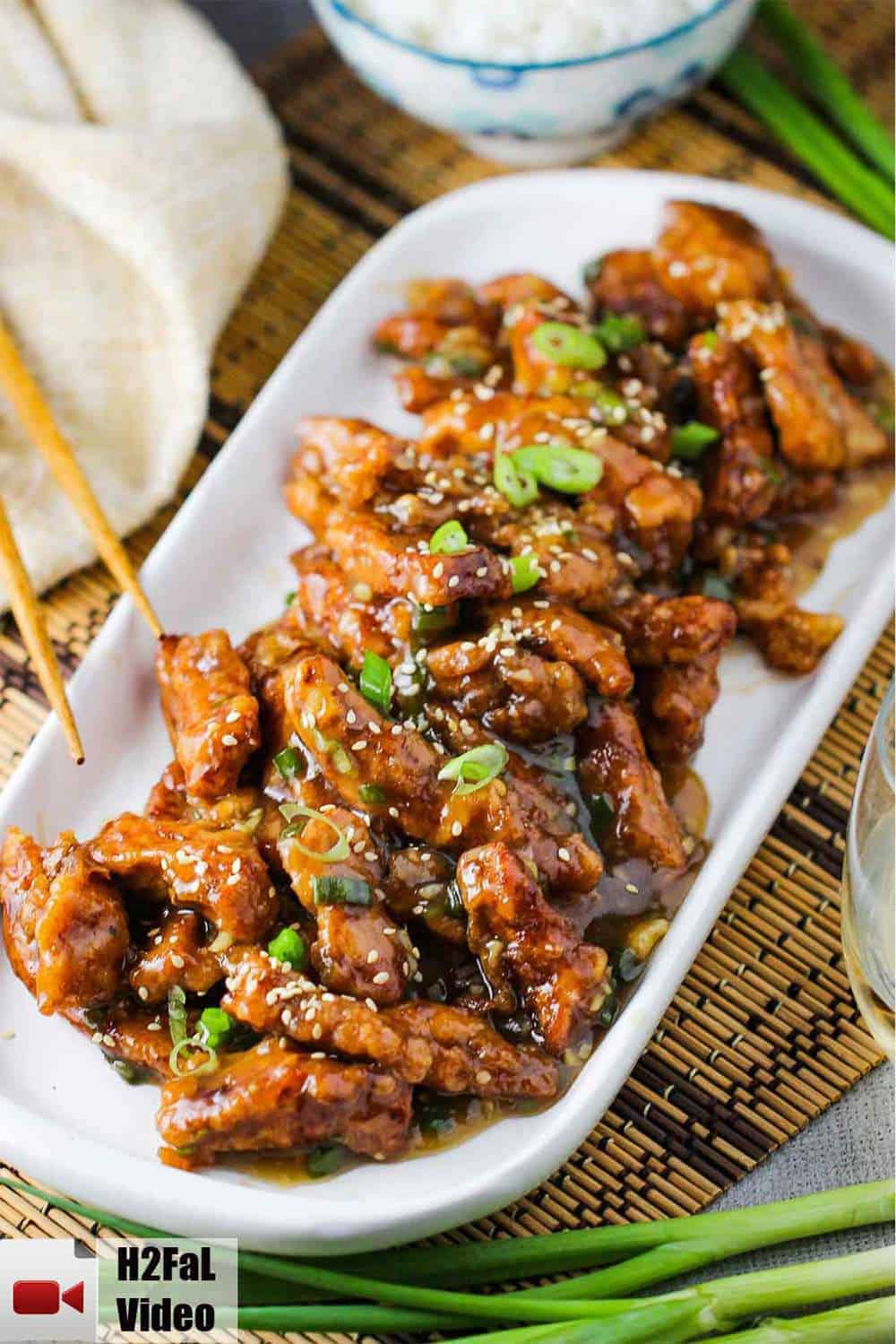 A long white platter filled with sweet and sour pork with chop sticks nearby. 