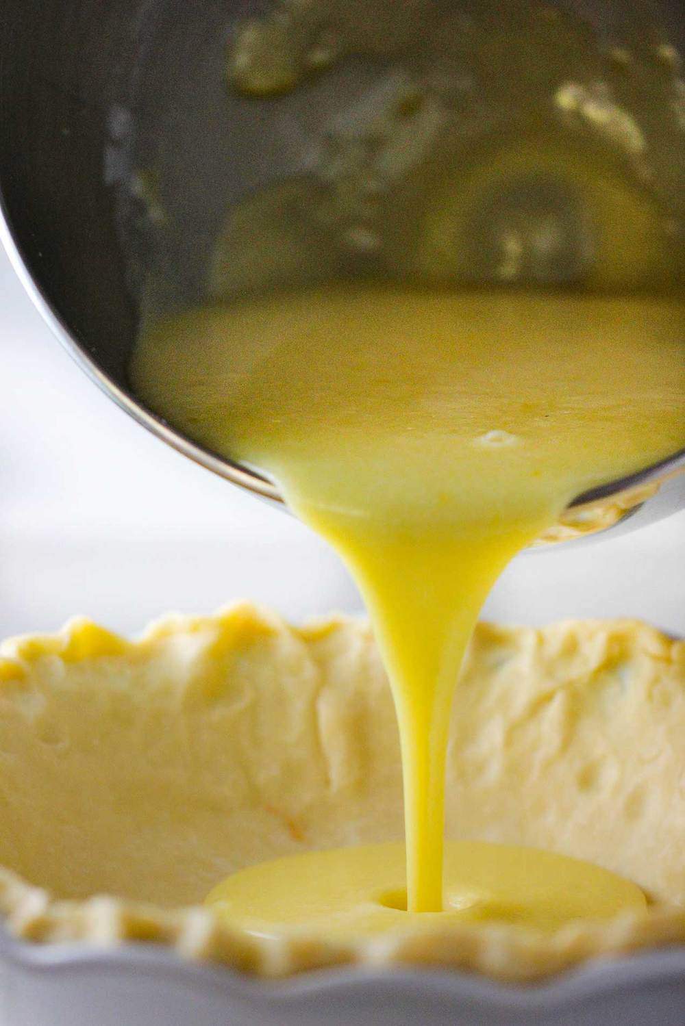 A bowl pouring custard into a pie shell.