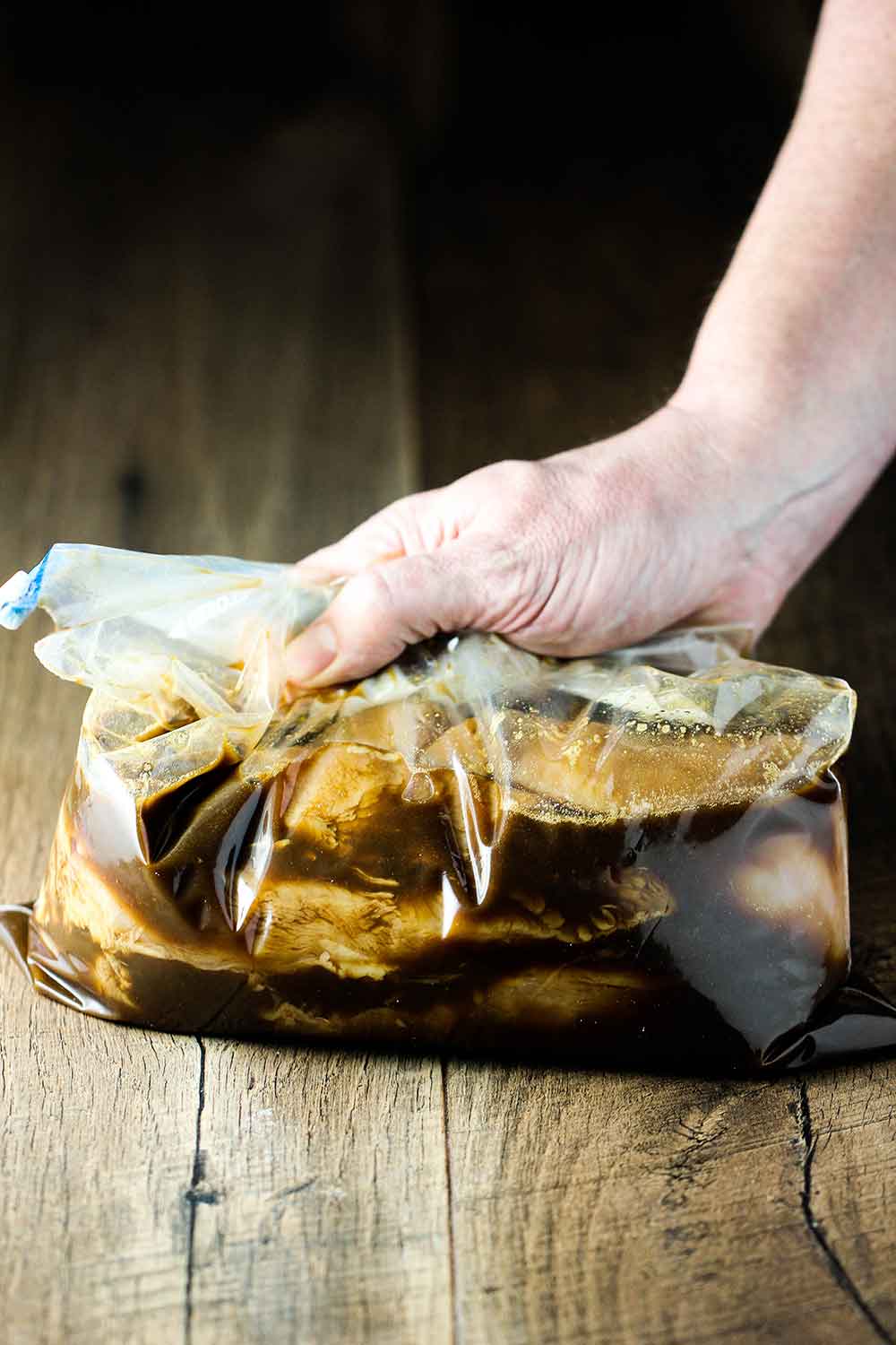 A large freezer baggie with chicken fajitas meat and marinade being pressed by a hand on a cutting board. 
