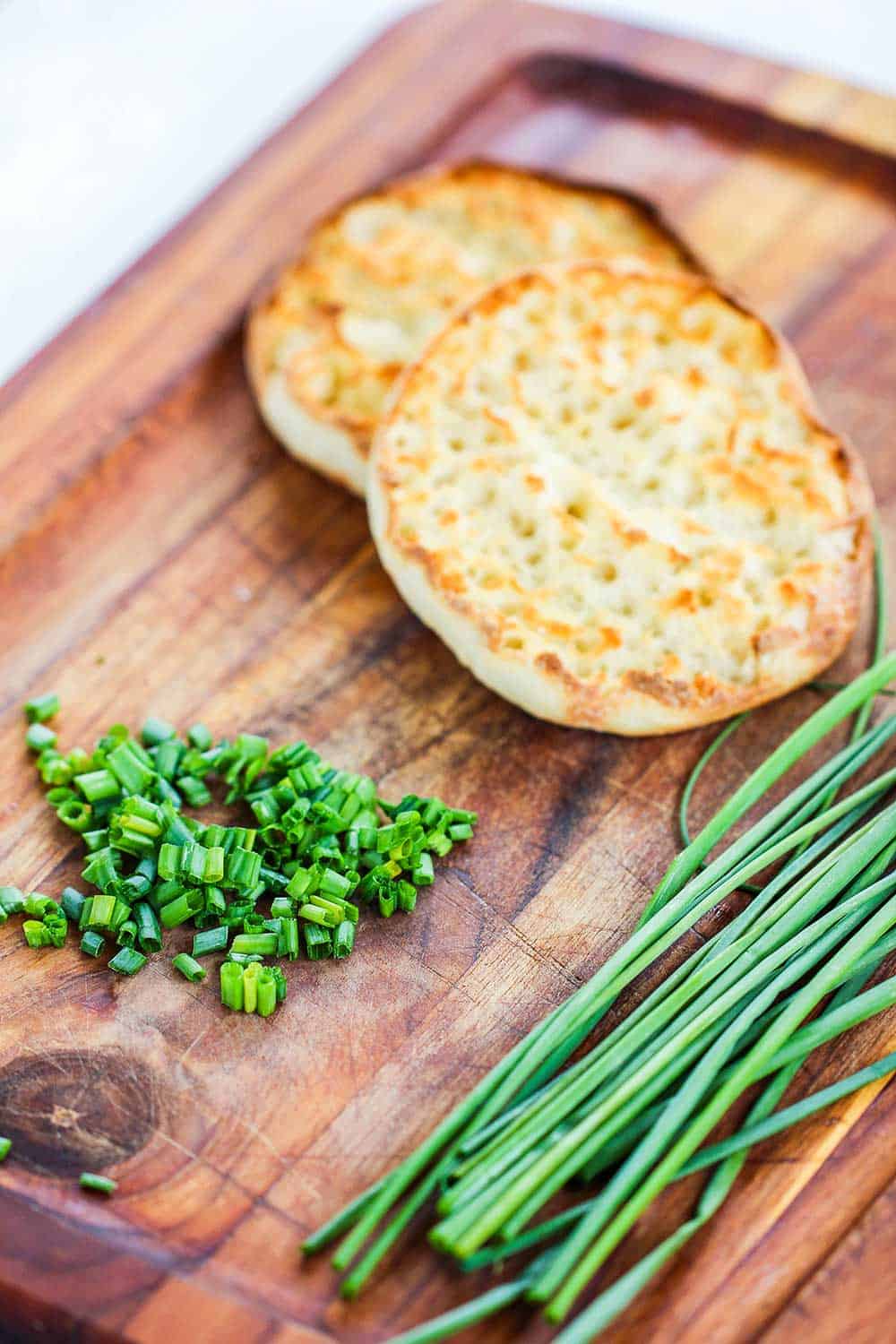 A taste English muffin on a cutting board next to snipped chives. 