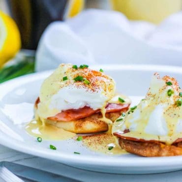 Classic Eggs Benedict on a white plate next to cups of coffee and orange juice.