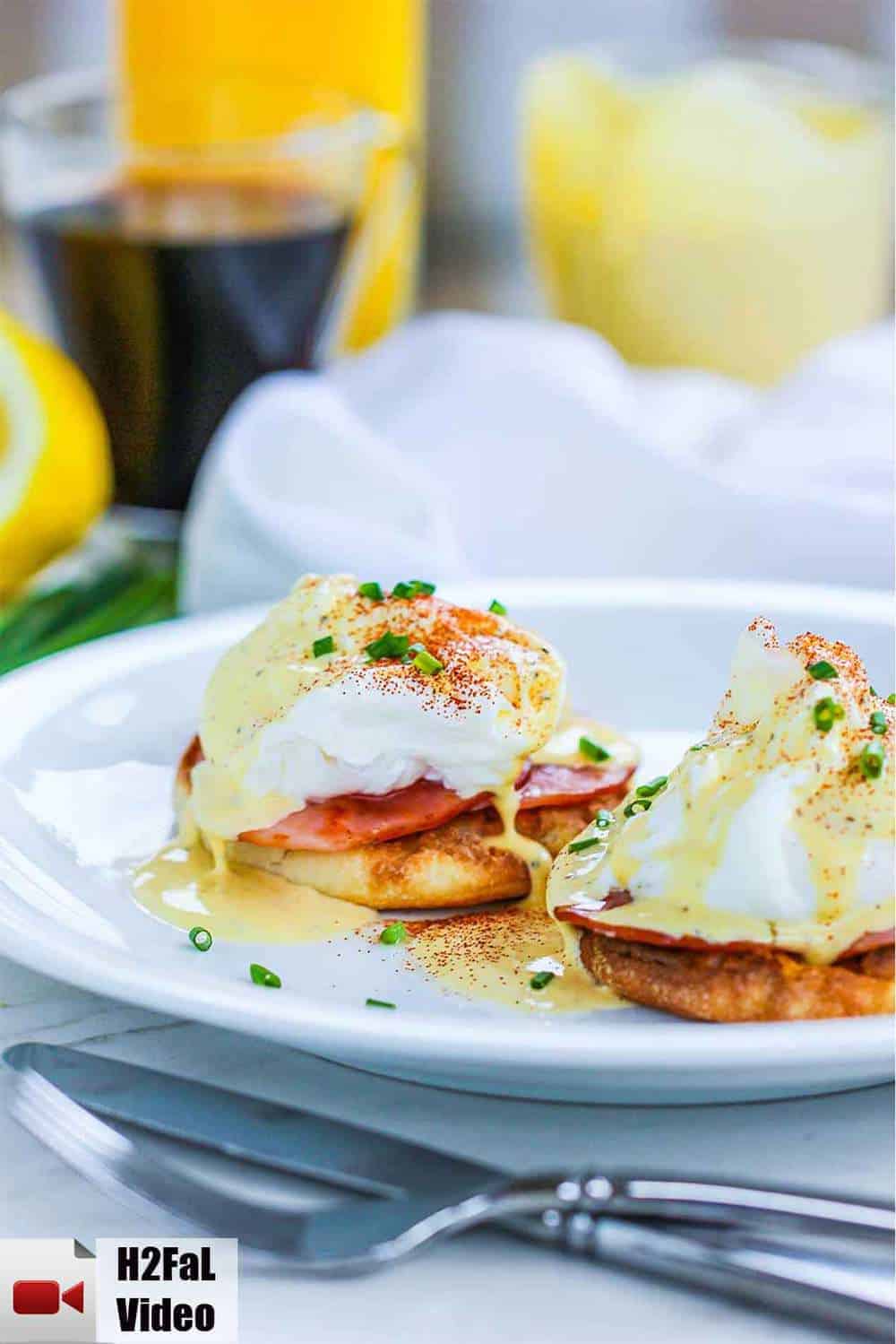 Classic eggs Benedict on a white plate next to cups of coffee and orange juice. 