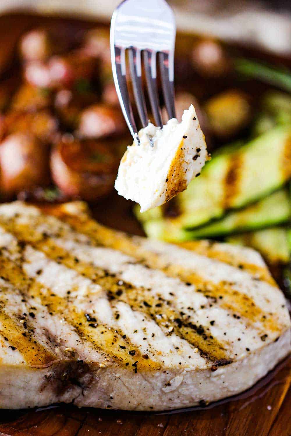 A fork holding a piece of grilled swordfish on a cutting board.