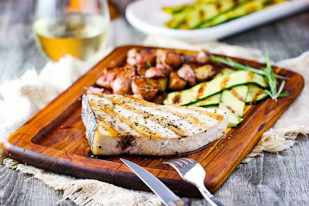 Grilled swordfish steaks on a cutting board with zucchini and baby potatoes