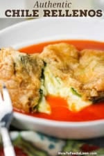 An authentic chile relleno that has been split open with melted cheese spilling out into a red sauce in a shallow bowl.