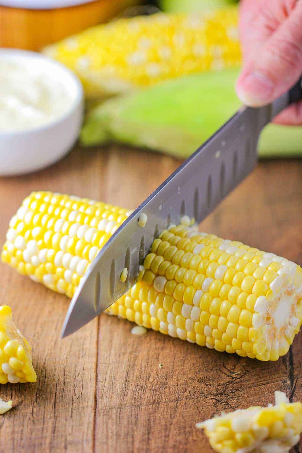 A sharp knife cutting corn in the middle for slow-cooker corn on the cob. 