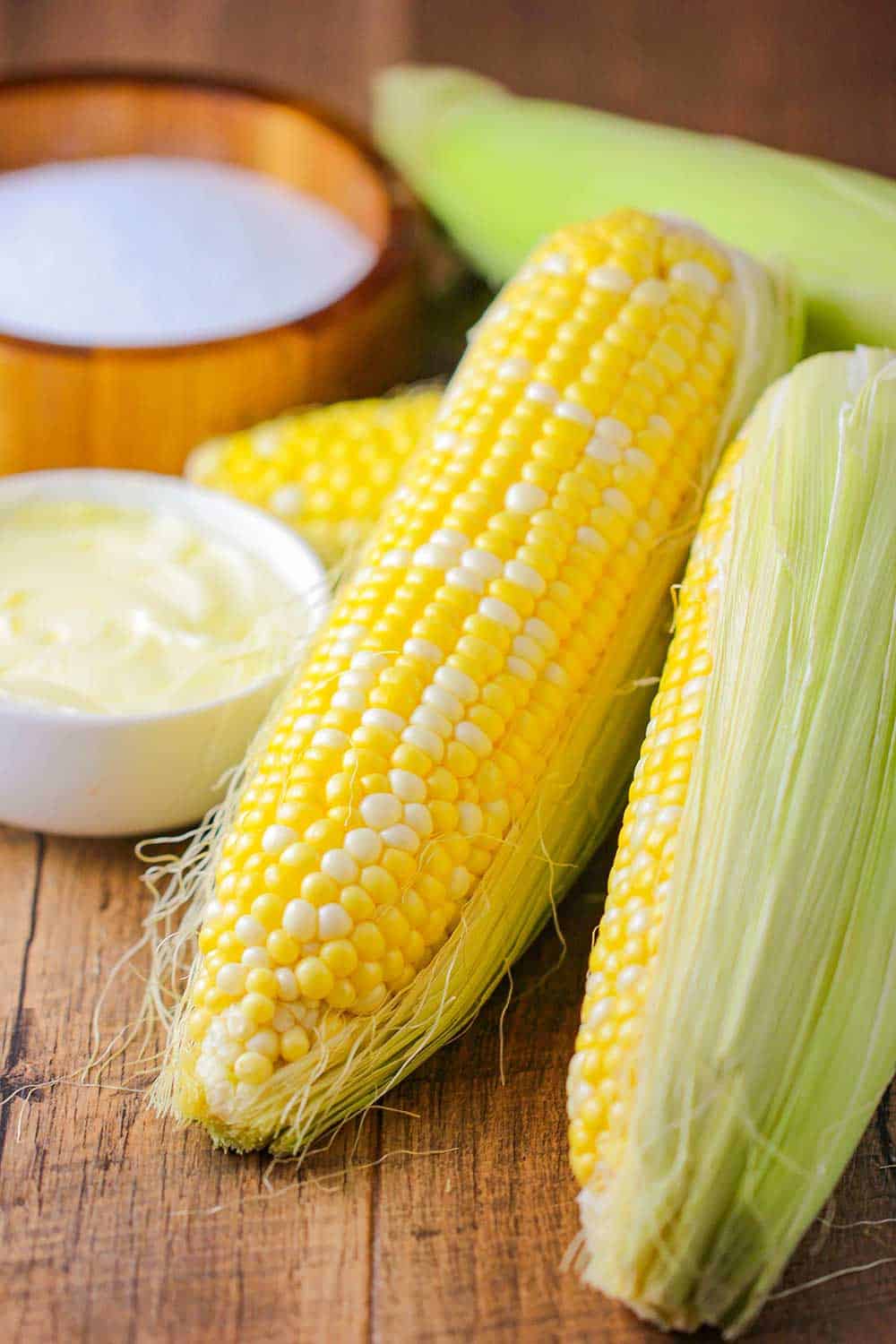 Partially shucked corn next to butter and salt.