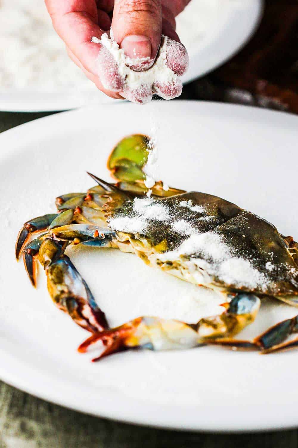 Fingers sprinkling flour over a soft-shell crab. 