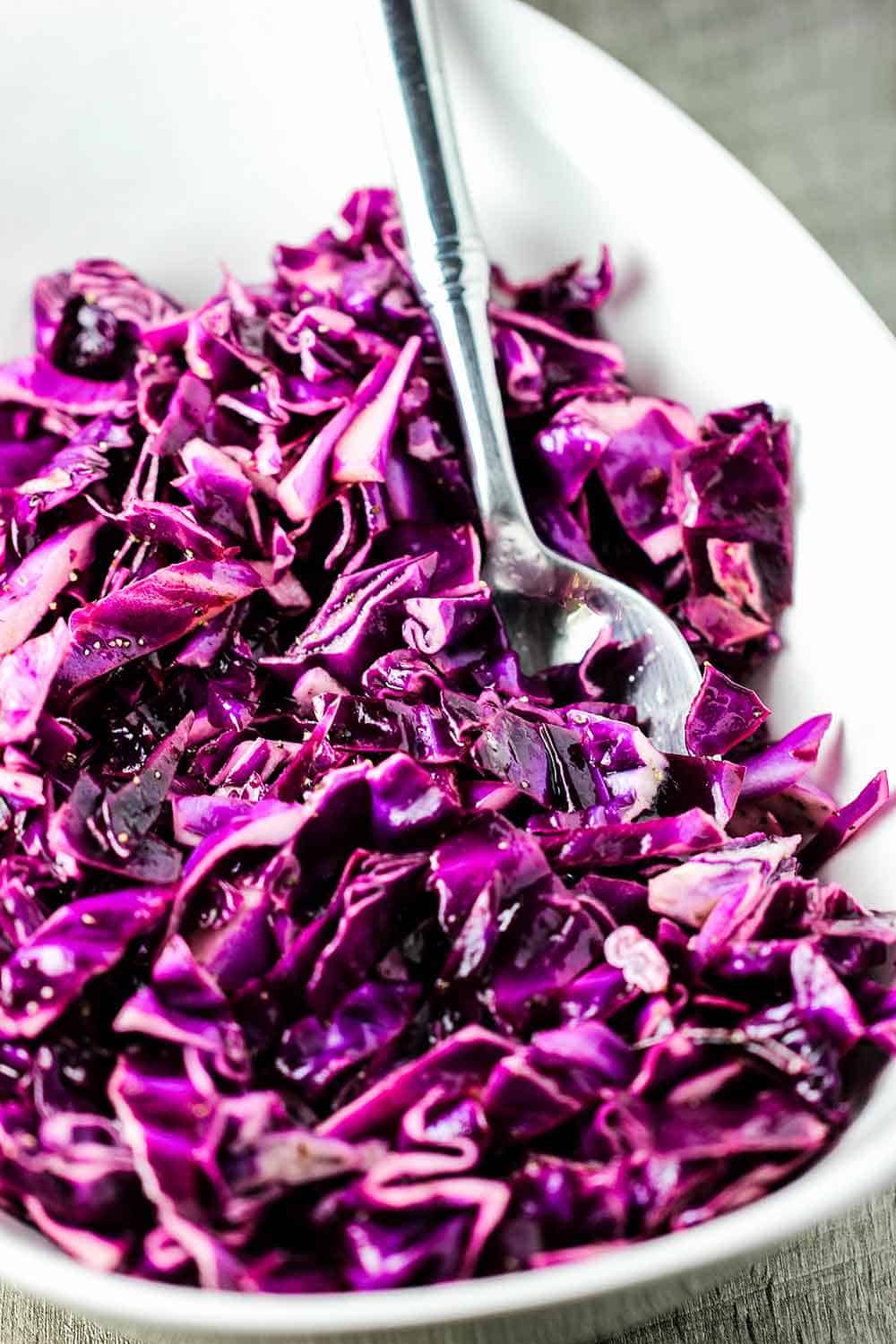 A white bowl of red cabbage slaw with a silver spoon.