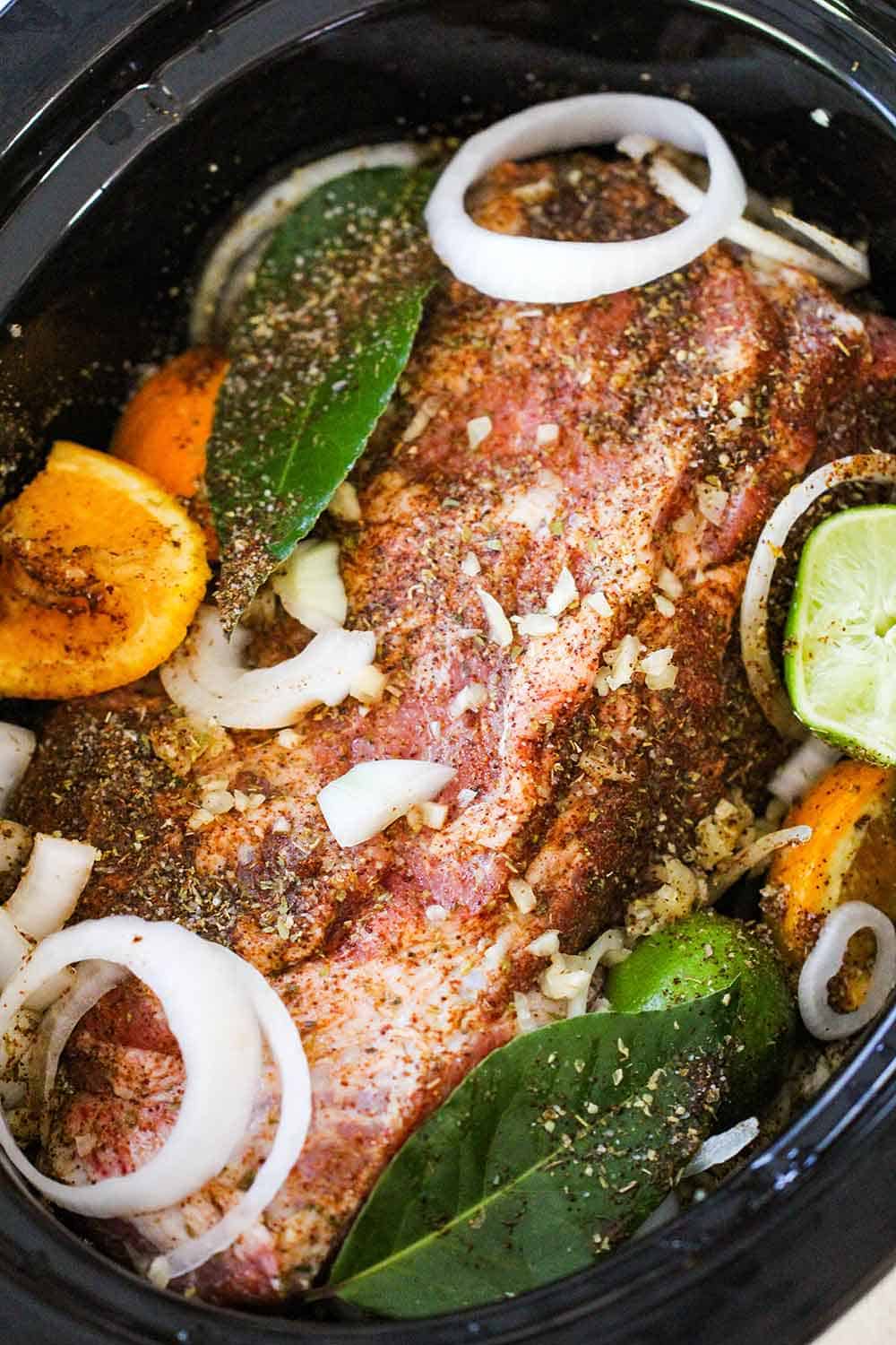 Place the pork shoulder into the slow cooker with aromatics, citrus and liquids.