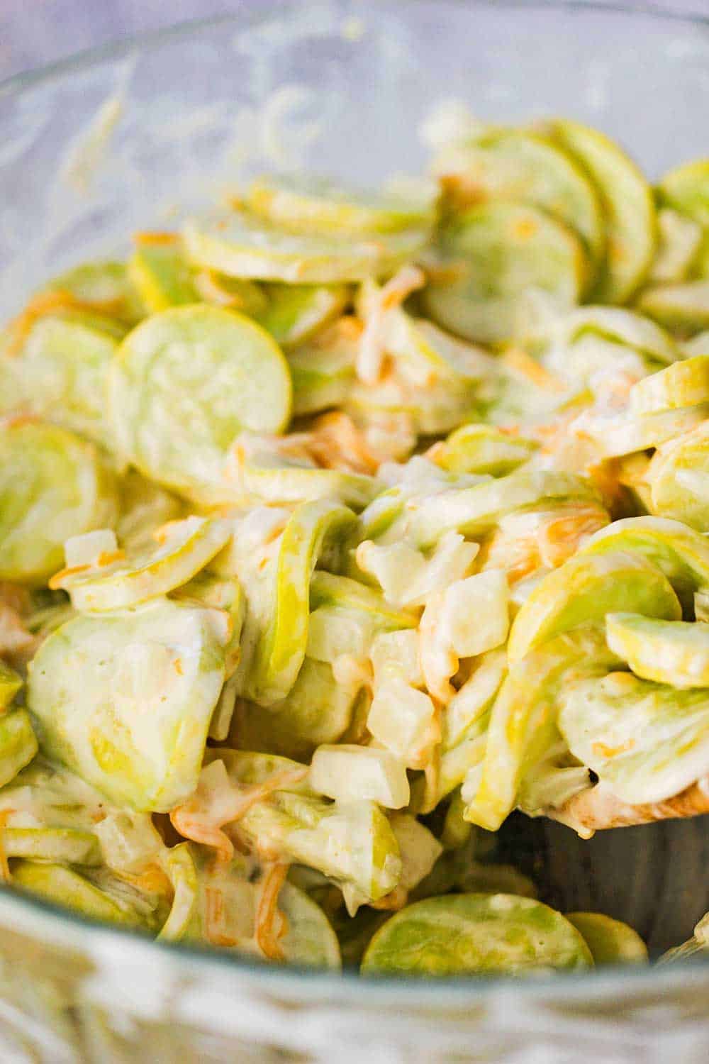 A large glass bowl with a cooked yellow squash, cheese and cream mixture for yellow squash casserole. 