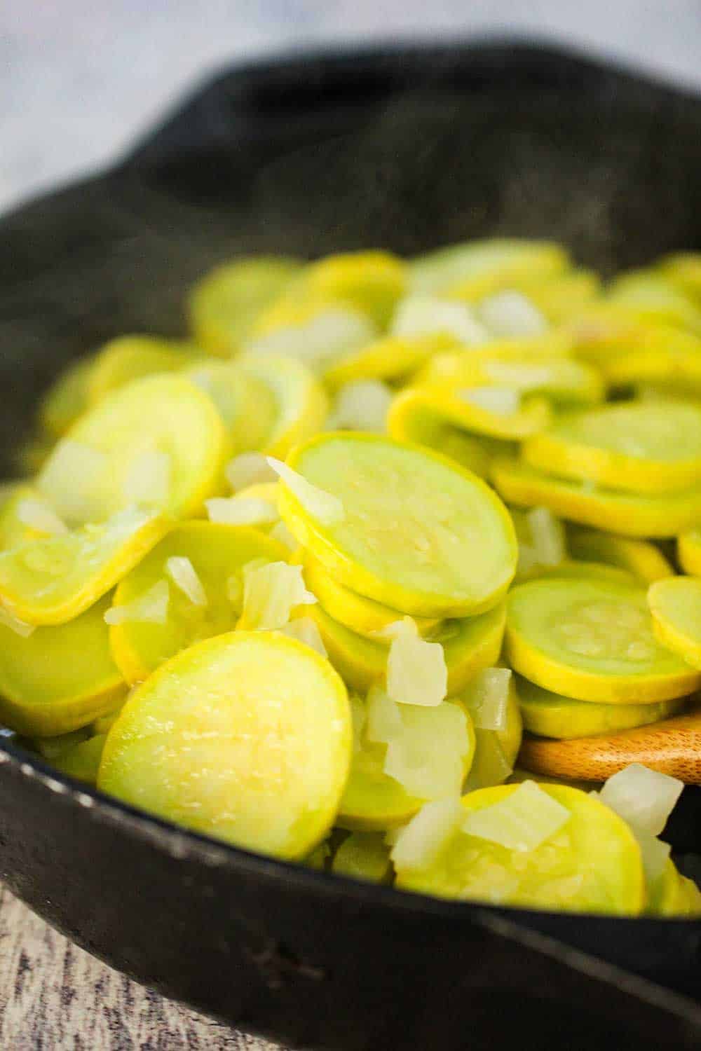 Yellow squash and chopped onion cooking in a large black cast iron skillet. 